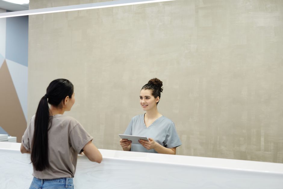 A patient checking in with a smiling receptionist holding a tablet