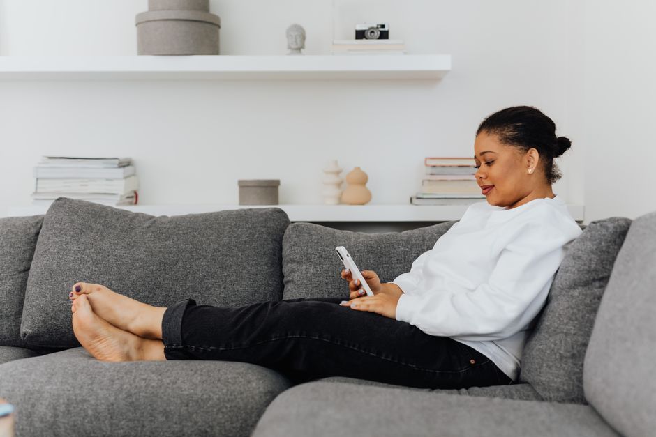 A patient relaxing on her couch while completing a form on her phone
